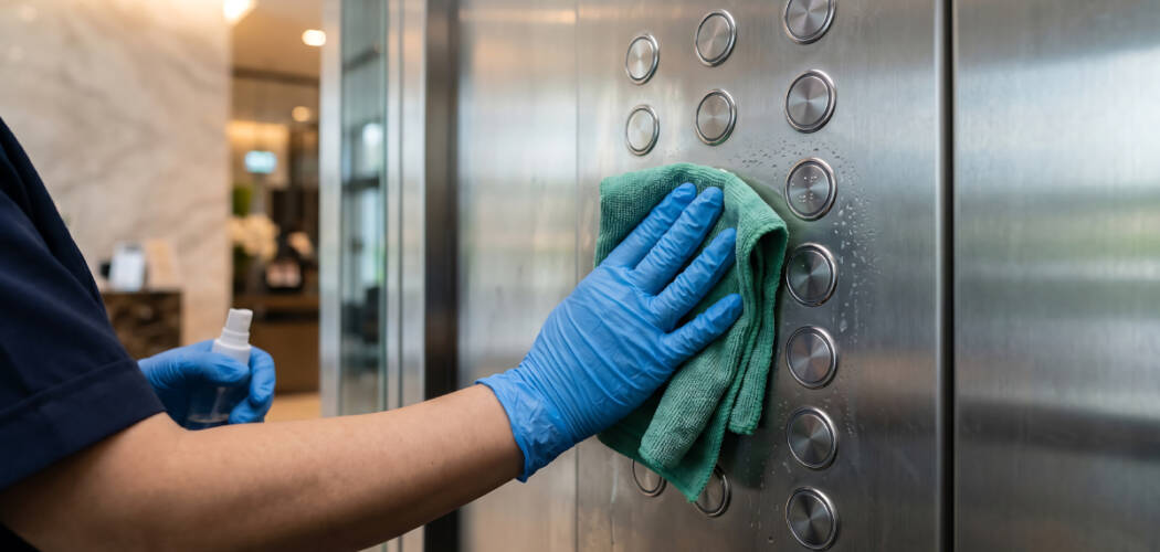 Professional janitor wiping down stainless steel elevator buttons during commercial cleaning in Mississauga.